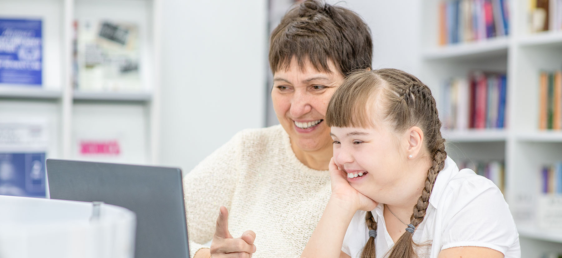 Happy teacher and smiling girl with down syndrome use a laptop a